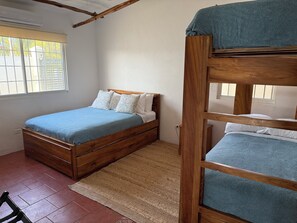 A bedroom with a wooden bunk bed, a single bed with a blue bedspread, a window with a view of palm trees, and a tiled floor. - 🌴 Private Beachfront Oasis in Playa Malibu 🌊 (Provincia de Panamá Oeste)