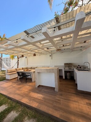 Un patio exterior con cocina integrada, zona de estar y una pérgola.