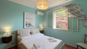 A bedroom with a bed, two bedside tables, a window with curtains, and a wall-mounted air conditioner. - Solemar Sicilia - Villa Elis (Bagheria)