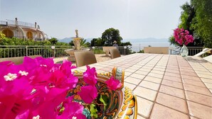 A terrace with a tiled floor, outdoor furniture, a decorative vase with flowers, and a view of the sea. - Solemar Sicilia - Villa Elis (Bagheria)