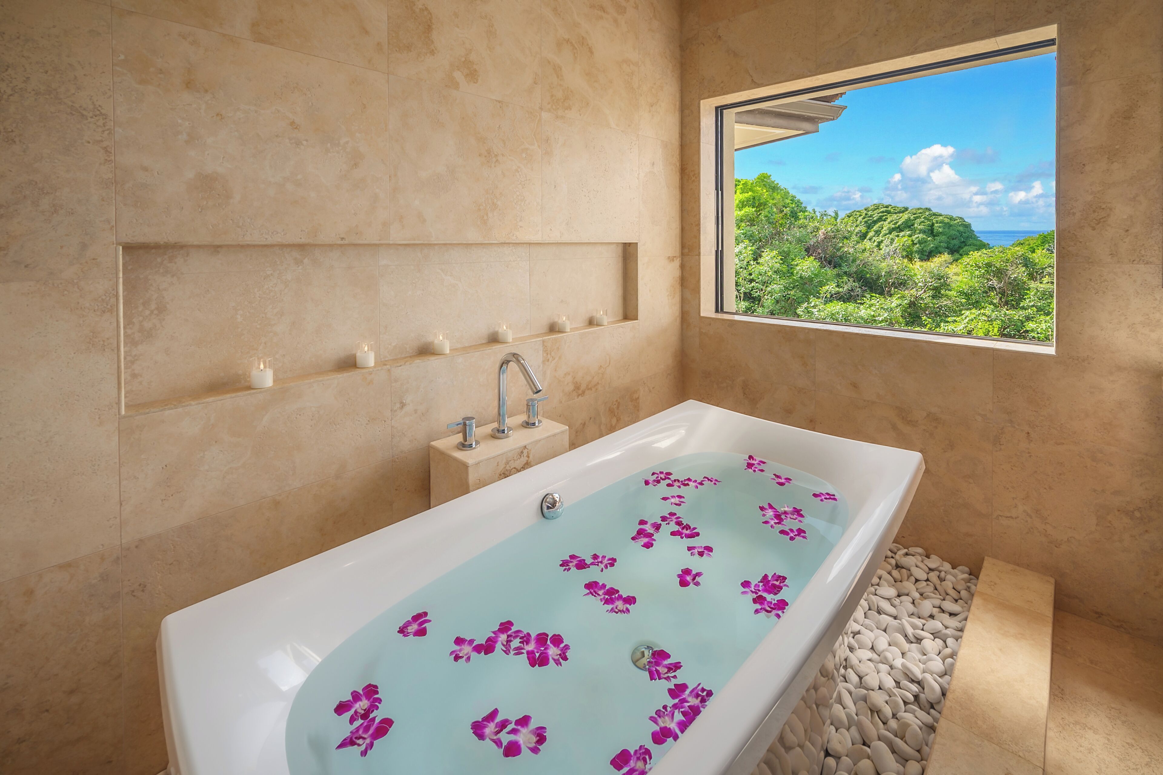 A modern bathroom with a freestanding bathtub, a window with a view of greenery, and a shelf with candles.