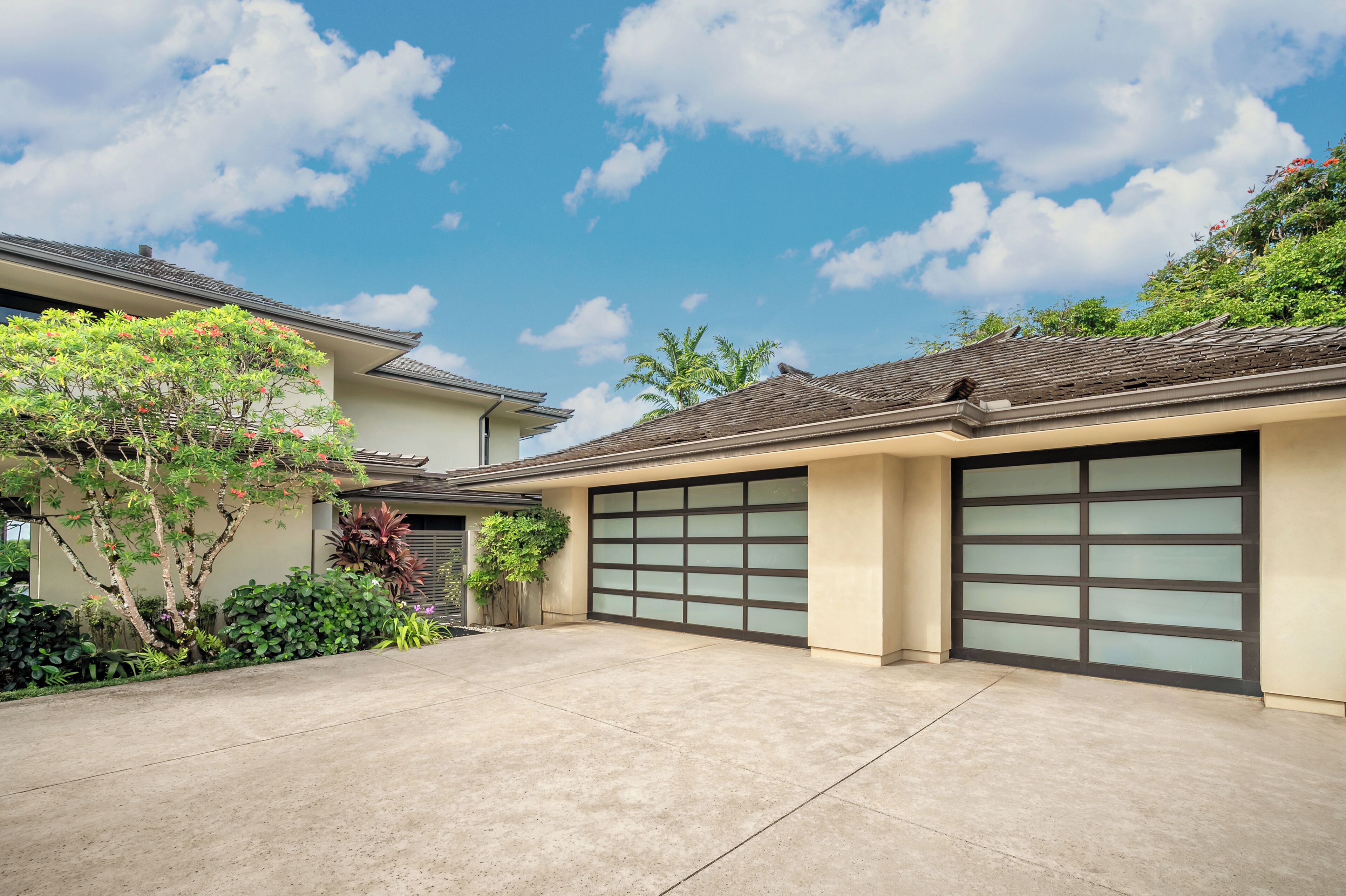 A residential garage with a concrete driveway, a garage door, and surrounding greenery.