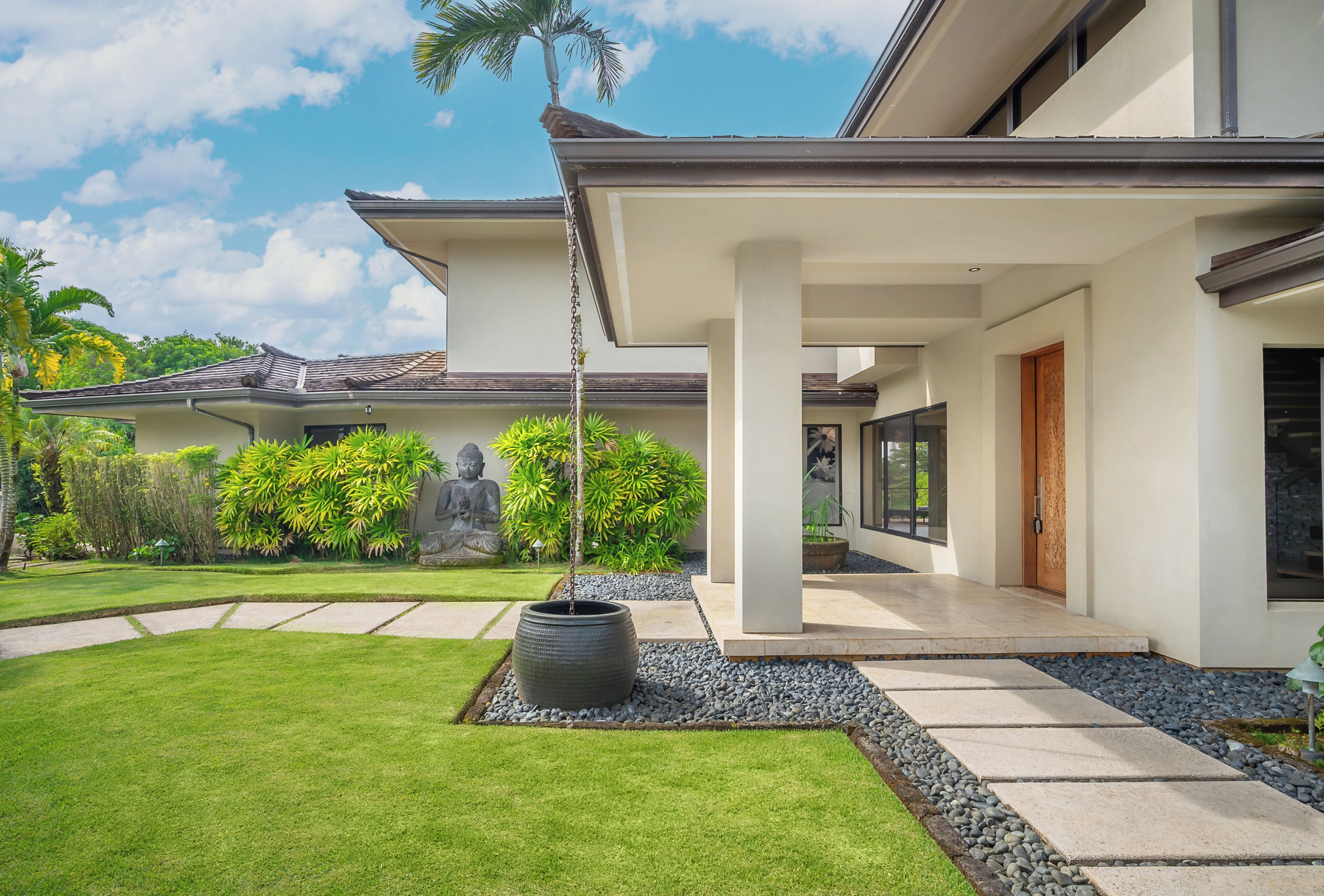 A modern house with a covered porch, a statue, and a well-maintained garden.