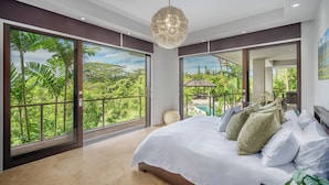 Een slaapkamer met een groot bed, uitzicht op weelderige begroeiing en een balkon.