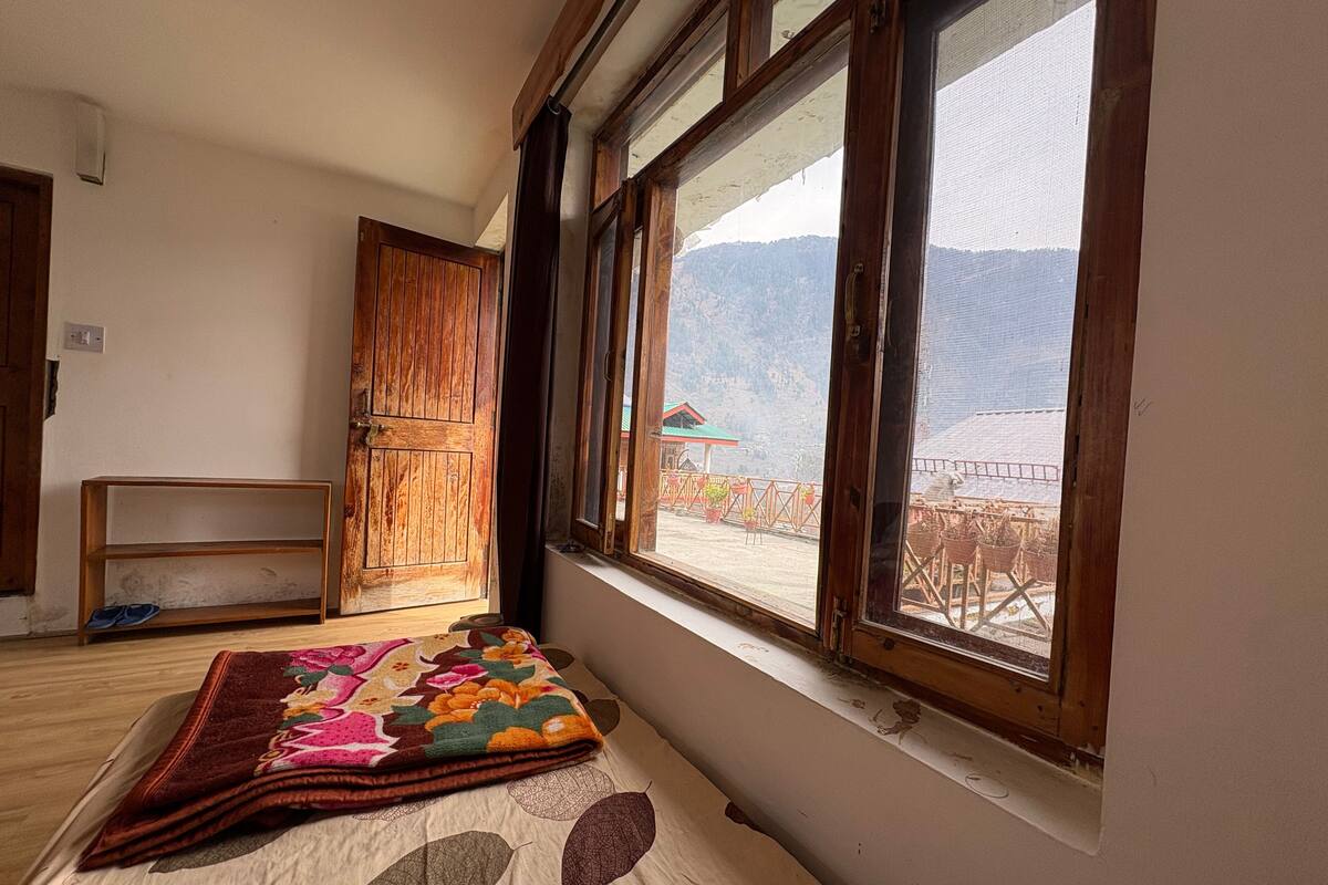 Una habitación con cama, una puerta de madera y ventana con vistas a una zona montañosa.