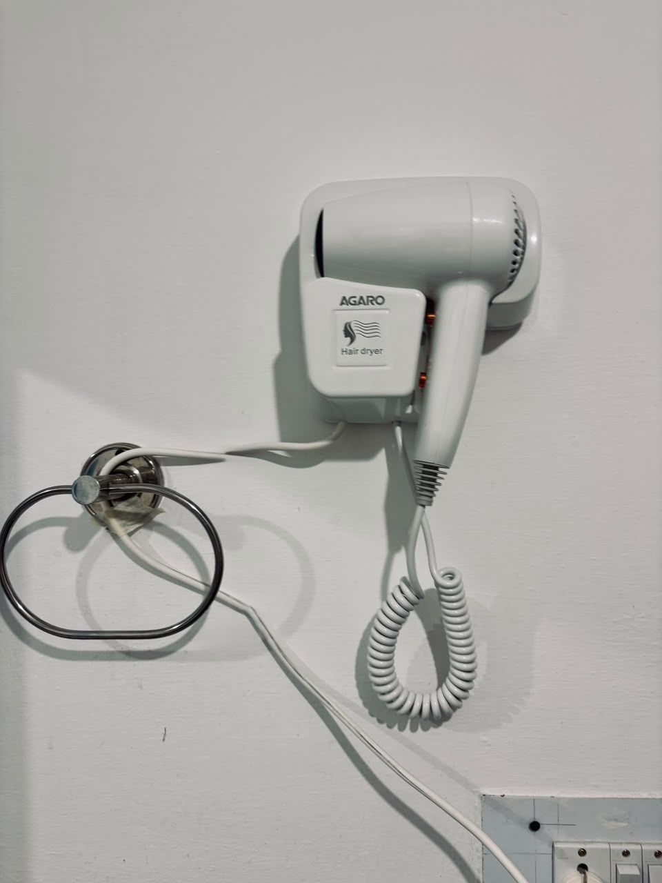 A hair dryer mounted on a wall with a cord and a plug.