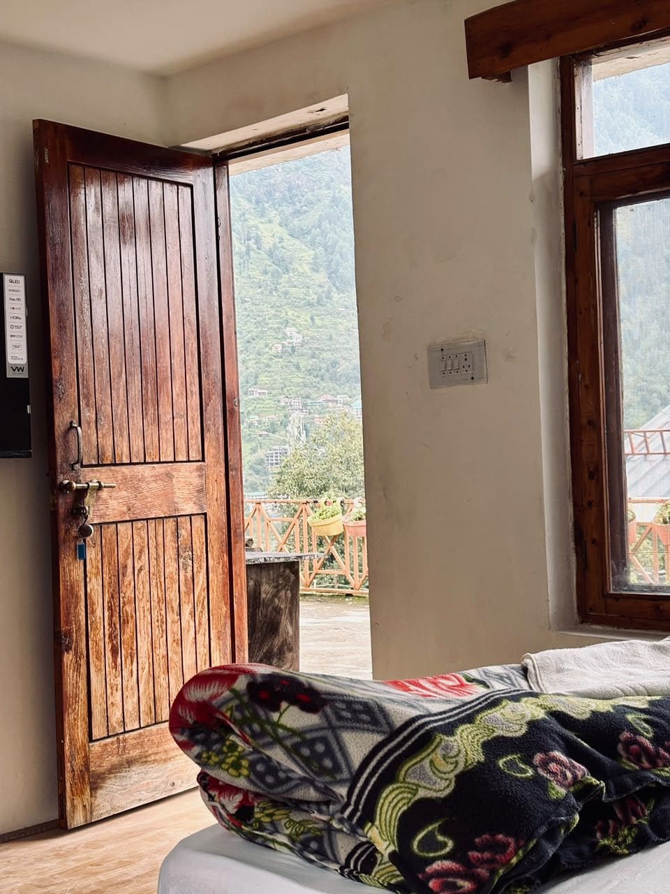 Una habitación con puerta de madera, una ventana y una cama con manta estampada.