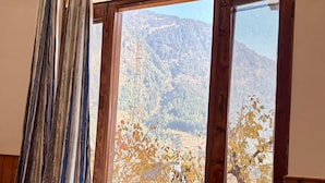 Ein Zimmer mit Holzwänden, einem Bett mit lila Decke und einem Fenster mit Bergblick.