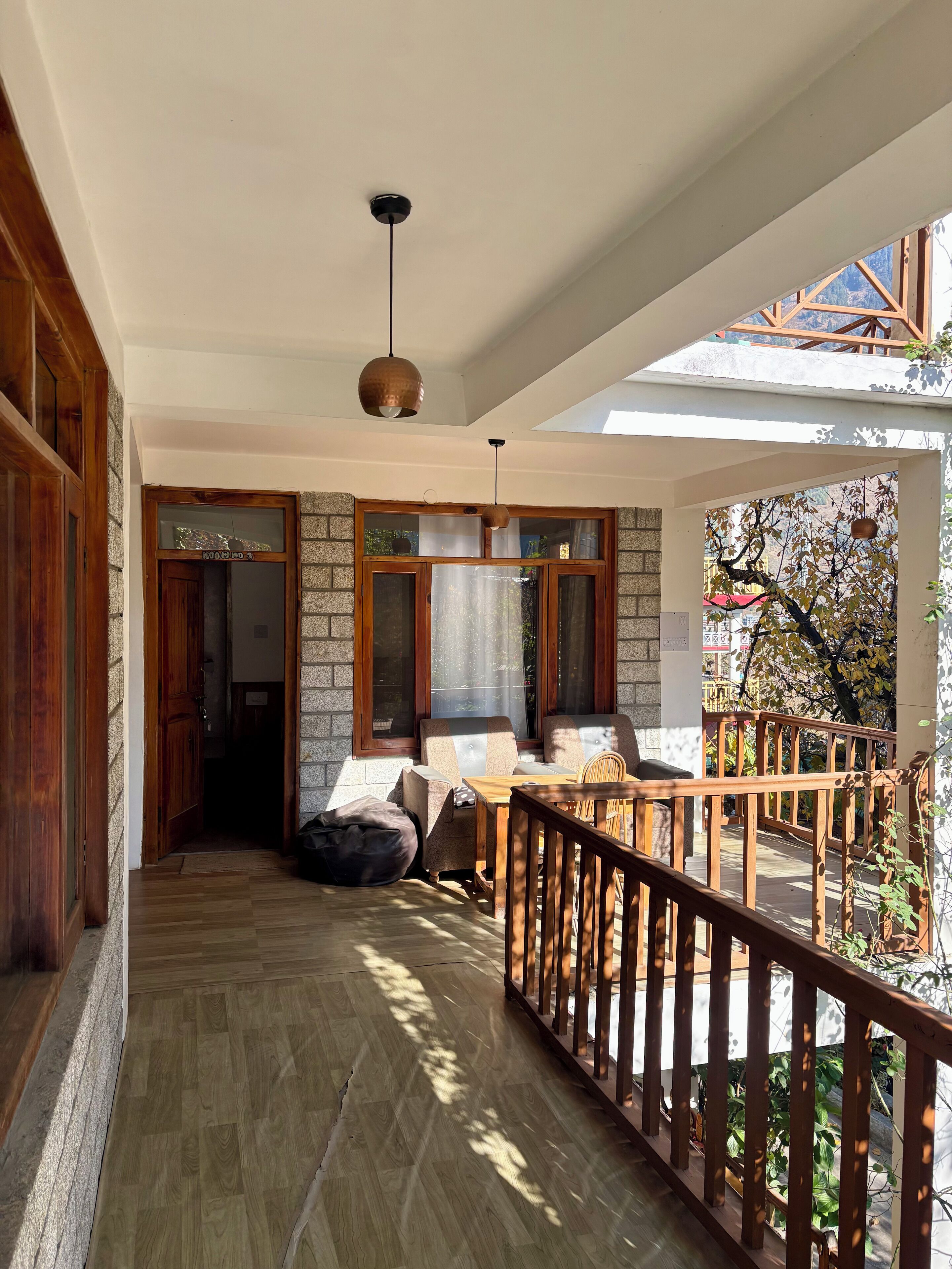 Corredor com piso de madeira que leva a uma área de estar com uma mesa e cadeiras, uma luminária pendente e vista para uma árvore pela janela.