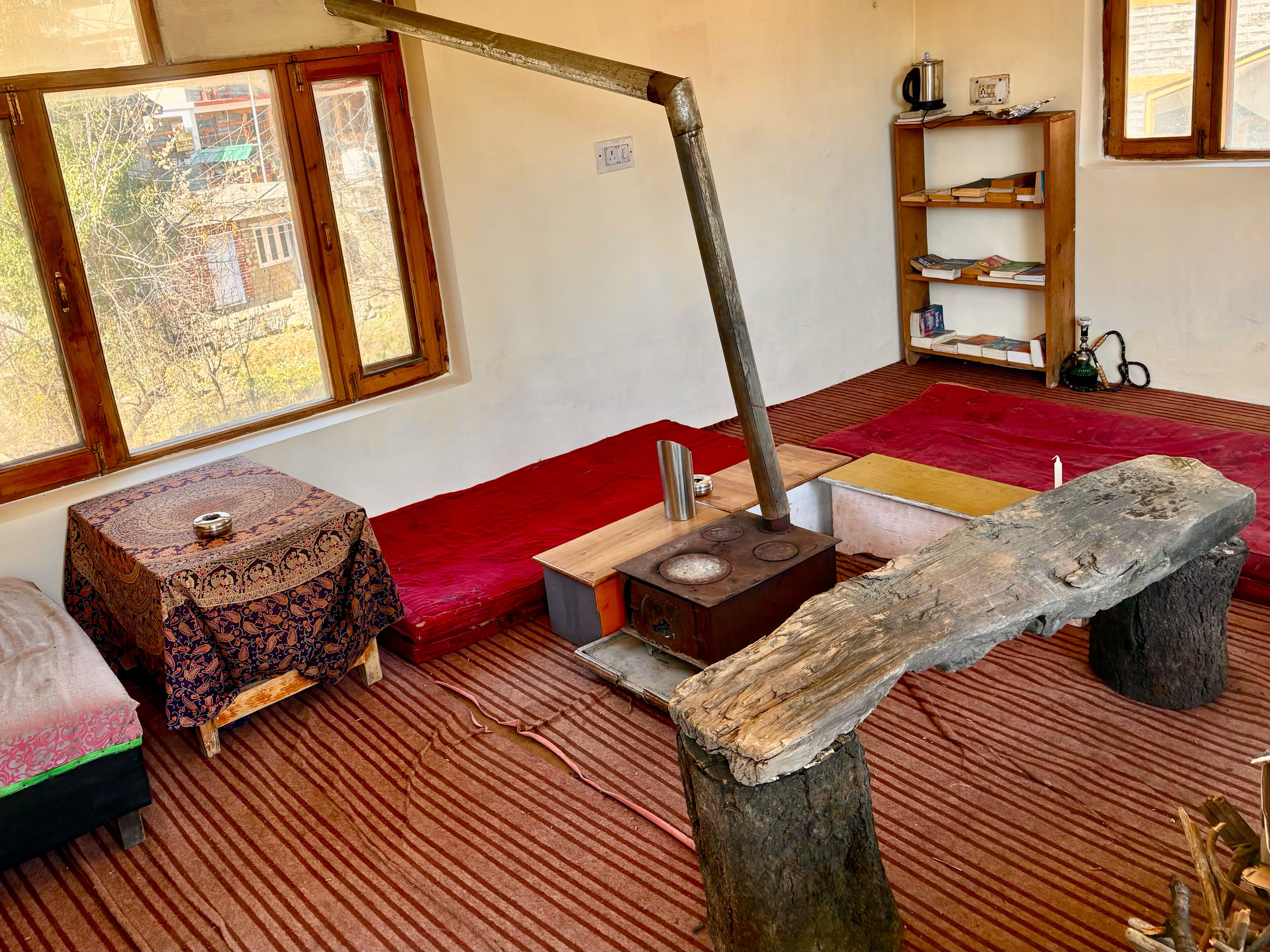 Um quarto com uma lareira tradicional, um sofá vermelho, um banquinho estampado e uma estante de livros.