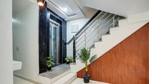A modern staircase with a wooden finish, a black marble wall, and a potted plant. - Hotel Solaris Retreat By The Arrow (New Delhi)