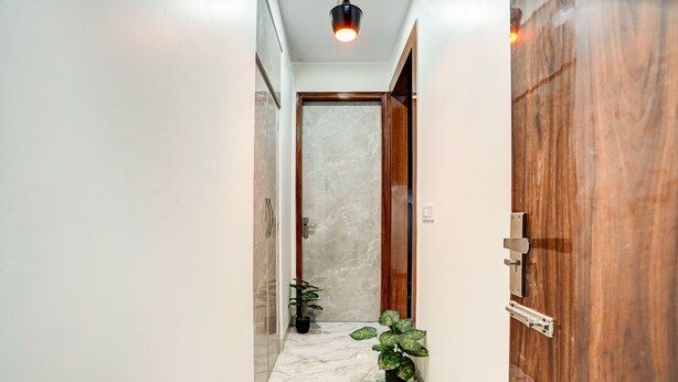 A hallway with marble flooring, wooden doors, and potted plants. - Hotel Solaris Retreat By The Arrow (New Delhi)