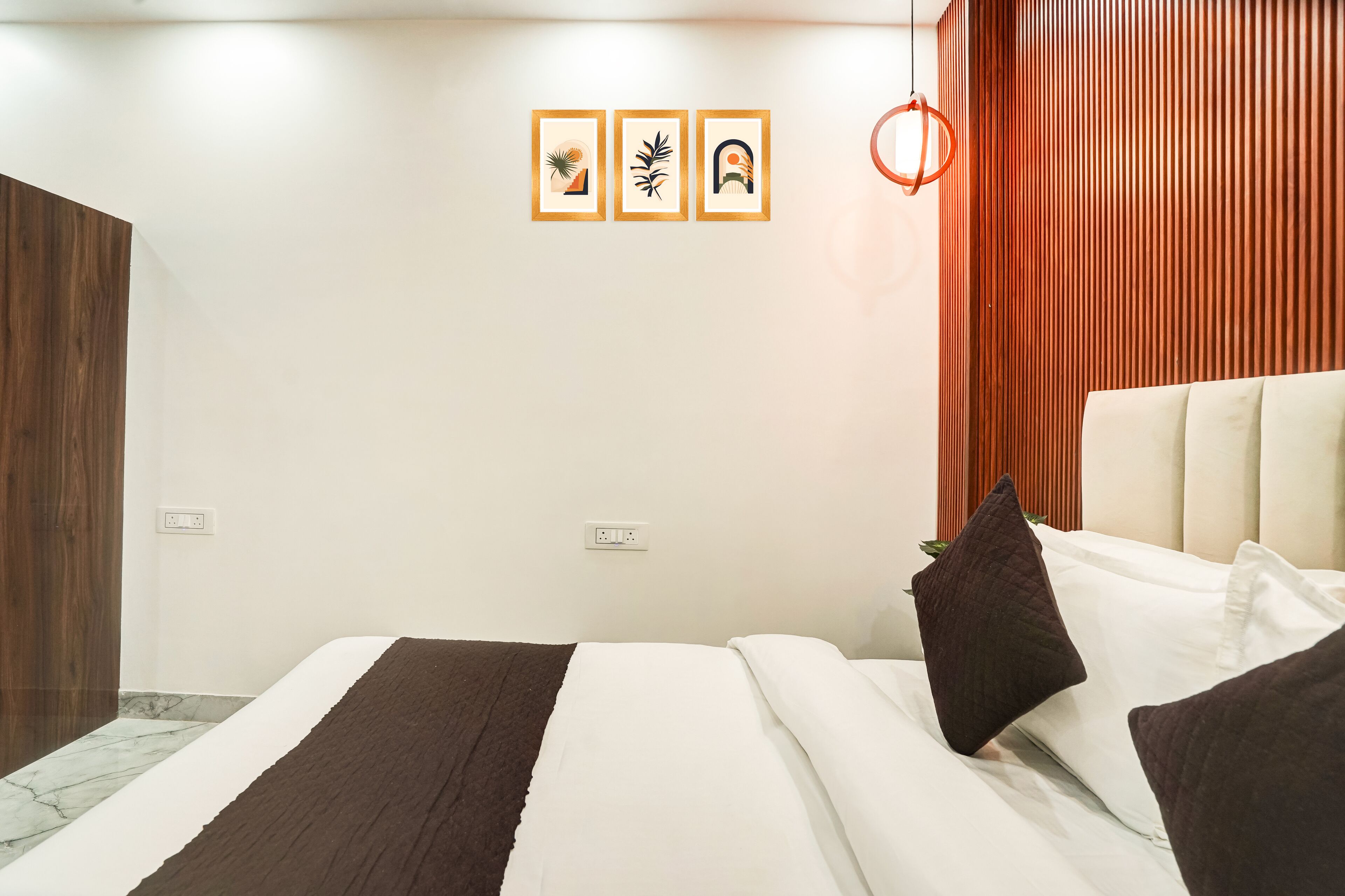 Une chambre d’hôtel moderne, équipée d’un lit, d’une armoire en bois et d’un mur orné de trois tableaux encadrés.