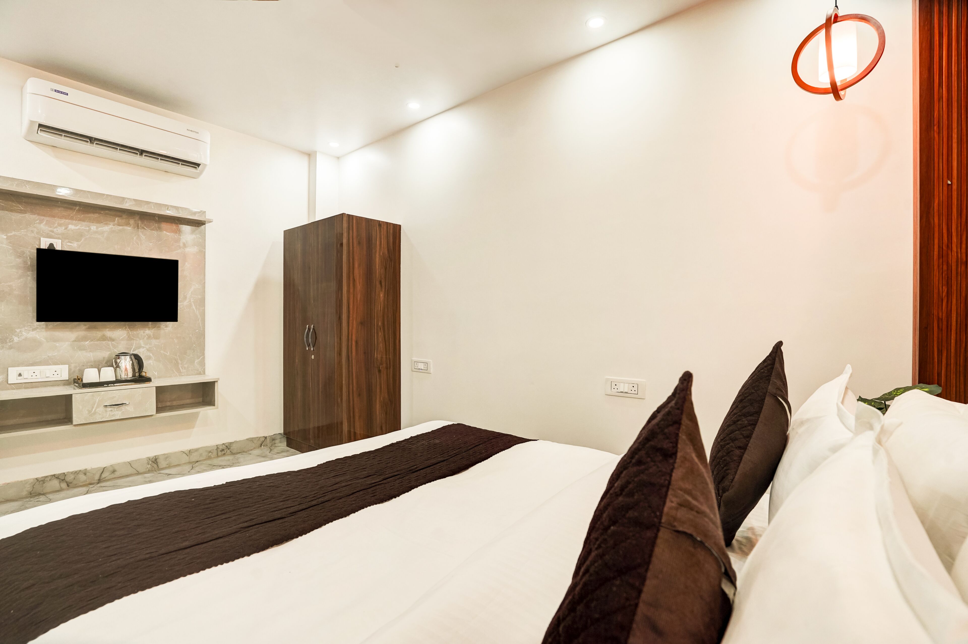 A modern hotel room with a bed, a wardrobe, a flat-screen TV mounted on a marble wall, and a ceiling light fixture.