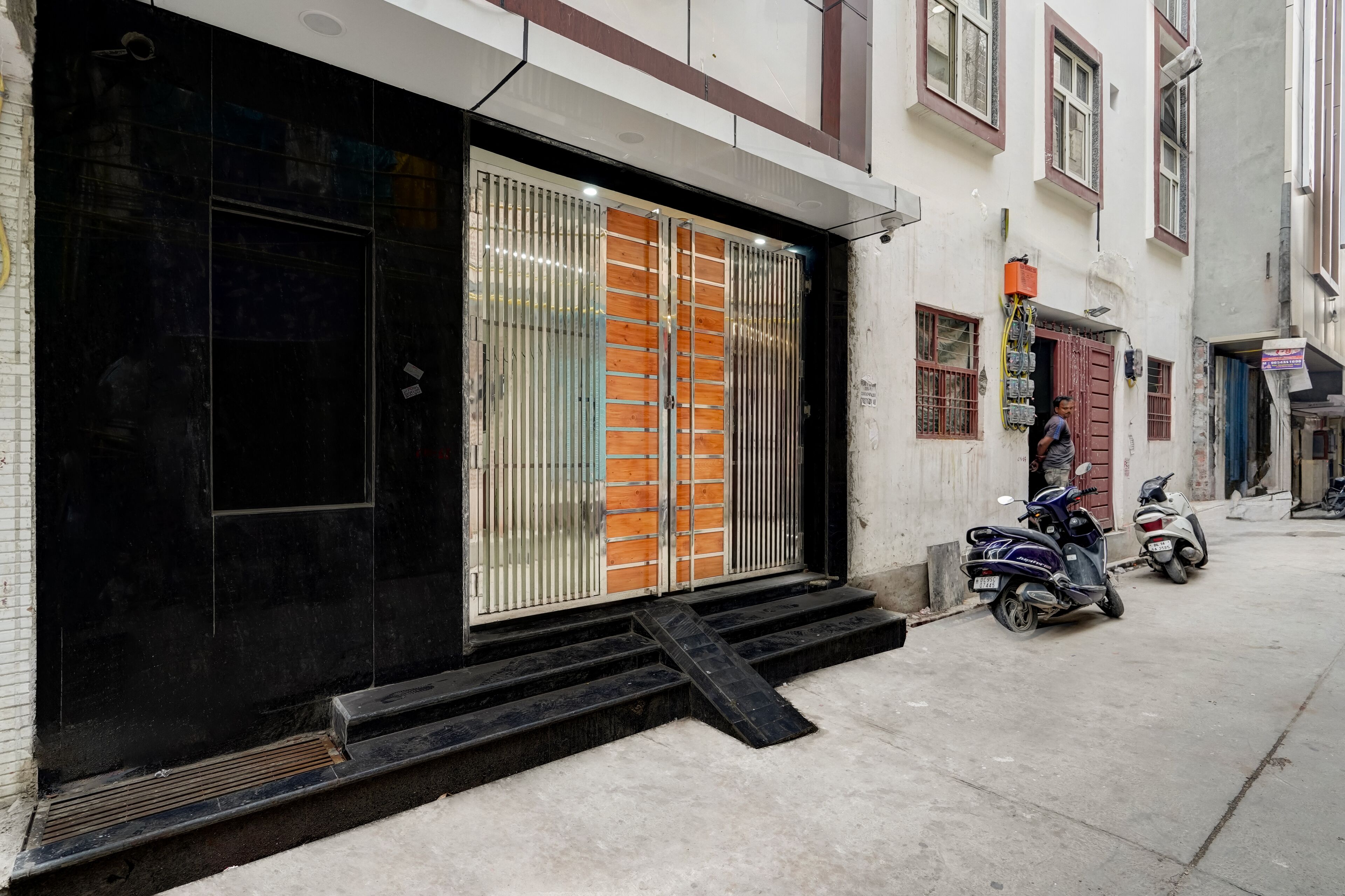 A building with a black entrance door, a set of steps leading up to the entrance, and two scooters parked outside.