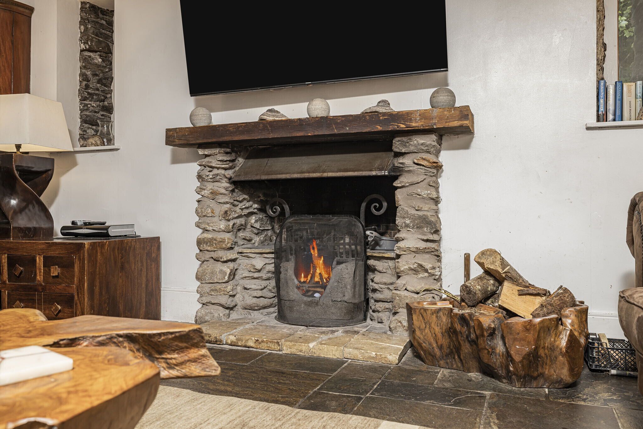 A stone fireplace with a fire, a wooden mantel, and a flat-screen TV above it.