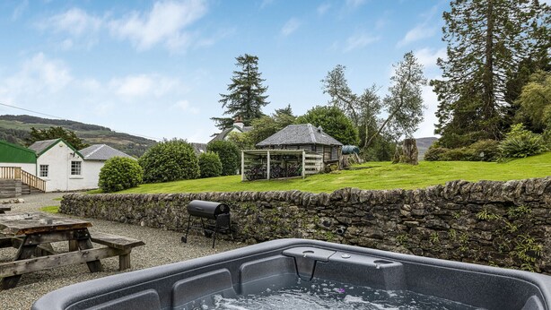 A hot tub in a garden with a stone wall, picnic table, and a gazebo in the background. - Old Barn at Ormidale House (Glendaruel)