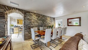 A dining area with a stone wall, a wooden table, and white chairs. - Old Barn at Ormidale House (Glendaruel)