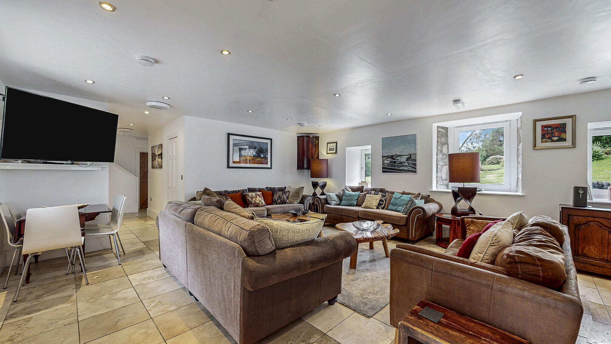 A spacious living room with a large sectional sofa, a flat-screen TV, and a dining area with a table and chairs.