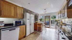 A modern kitchen with wooden cabinets, a built-in microwave, a refrigerator, and a stone accent wall. - Old Barn at Ormidale House (Glendaruel)