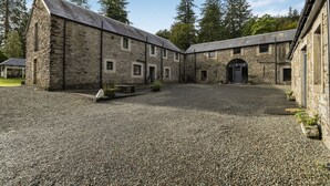 A stone building with a gravel courtyard and a covered walkway. - Old Barn at Ormidale House (Glendaruel)