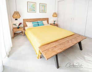 Ein Schlafzimmer mit einem Holzbett, einer gelben Decke, zwei gerahmten Kunstwerken an der Wand und einem Nachttisch mit einer Lampe.