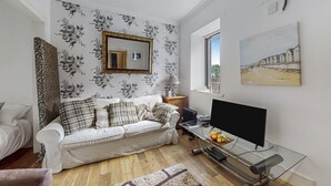 Ein Wohnzimmer mit einem weißen Sofa, einem Flachbildfernseher und Holzboden.