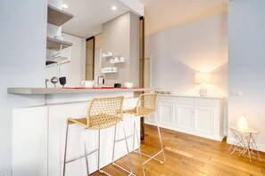 Una cocina moderna con armarios blancos, encimera de madera, dos taburetes de mimbre y una pequeña mesa redonda con una lámpara.