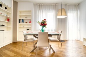 A dining area with a table, chairs, a vase of flowers, a lamp, and a bookshelf.