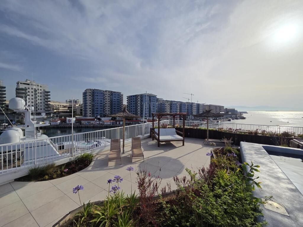 Una terraza en la azotea con una zona de estar, vistas al mar y edificios modernos al fondo.