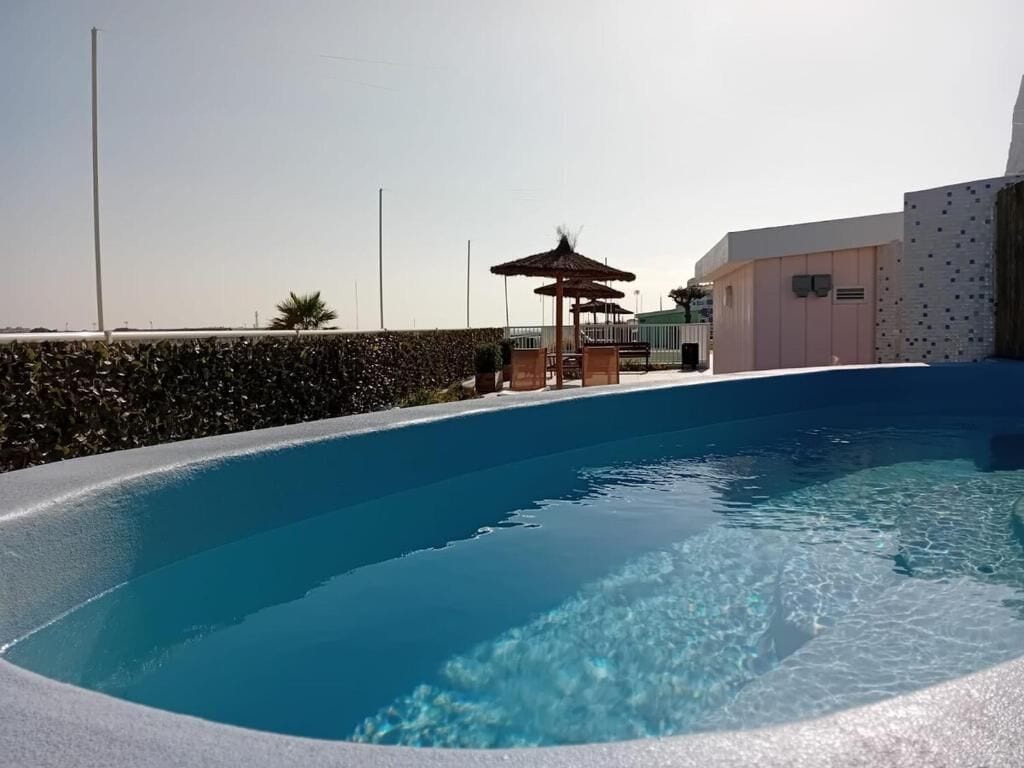 Una piscina con agua cristalina azul, un área de descanso con sillas y un edificio de diseño moderno.