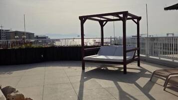 Un espacio al aire libre iluminado por el sol, con una pérgola de madera y un banco acolchado.