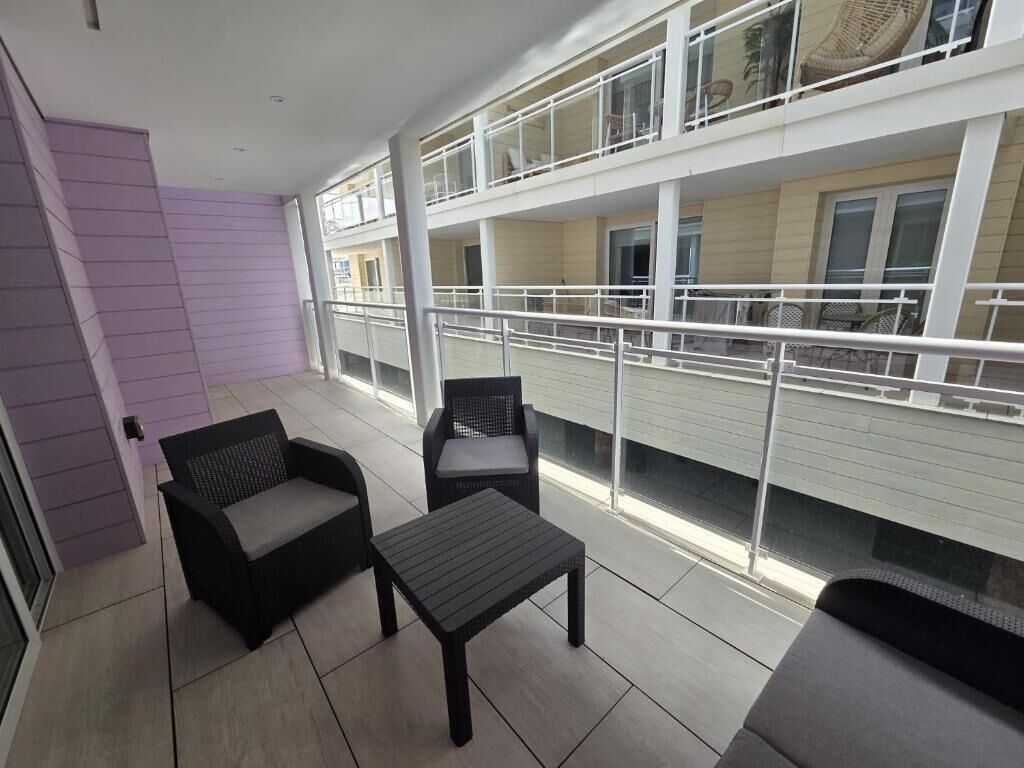 Un balcón con dos sillas y una mesa pequeña, con vista a un edificio con varios balcones.