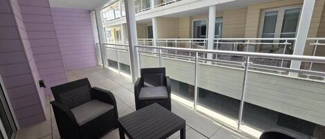 Un balcón con dos sillas y una mesa pequeña, con vista a un edificio con varios balcones.