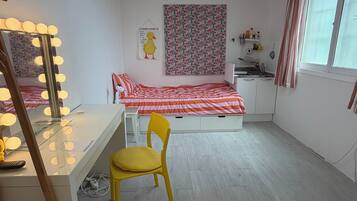 A bedroom with a bed, a desk with a mirror, a chair, a window, and a ceiling light.