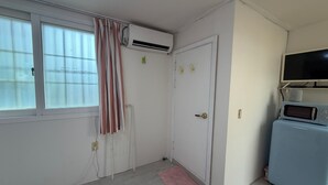 A room with a white door, a window with curtains, a small pink rug, a white radiator, and a blue appliance with a screen. - POOH_Serene studio with AC in charming Ewha Univ. (Seodaemun-gu,)