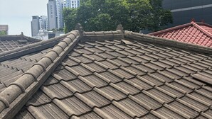 A traditional tiled roof with a stone balustrade, modern buildings in the background, and a tree providing shade. - POOH_Serene studio with AC in charming Ewha Univ. (Seodaemun-gu,)