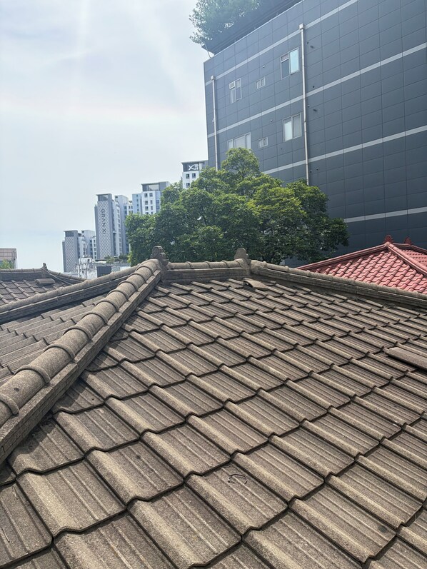 A traditional tiled roof with a stone balustrade, modern buildings in the background, and a tree providing shade. - POOH_Serene studio with AC in charming Ewha Univ. (Seodaemun-gu,)