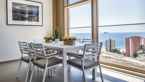 A dining area with a table and chairs, a framed picture on the wall, and a view of the sea and buildings. - Intempo by Holuxe - 034 - 3rd floor (Benidorm)