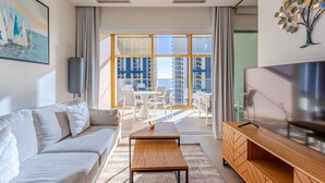 Een moderne woonkamer met een bank, salontafel, televisie en een balkon met uitzicht op gebouwen.