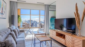 Ein modernes Wohnzimmer mit einer Couch, Fernseher und Blick auf die Stadt.