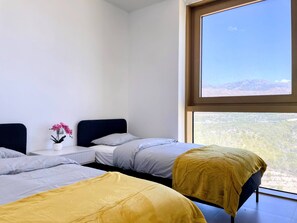 Een kamer met twee bedden, een tafeltje met een bloevas en een groot raam met uitzicht op de bergen.