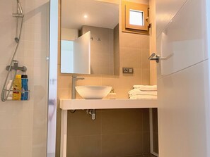 Een moderne badkamer met een witte wastafel, een spiegel en een douche.