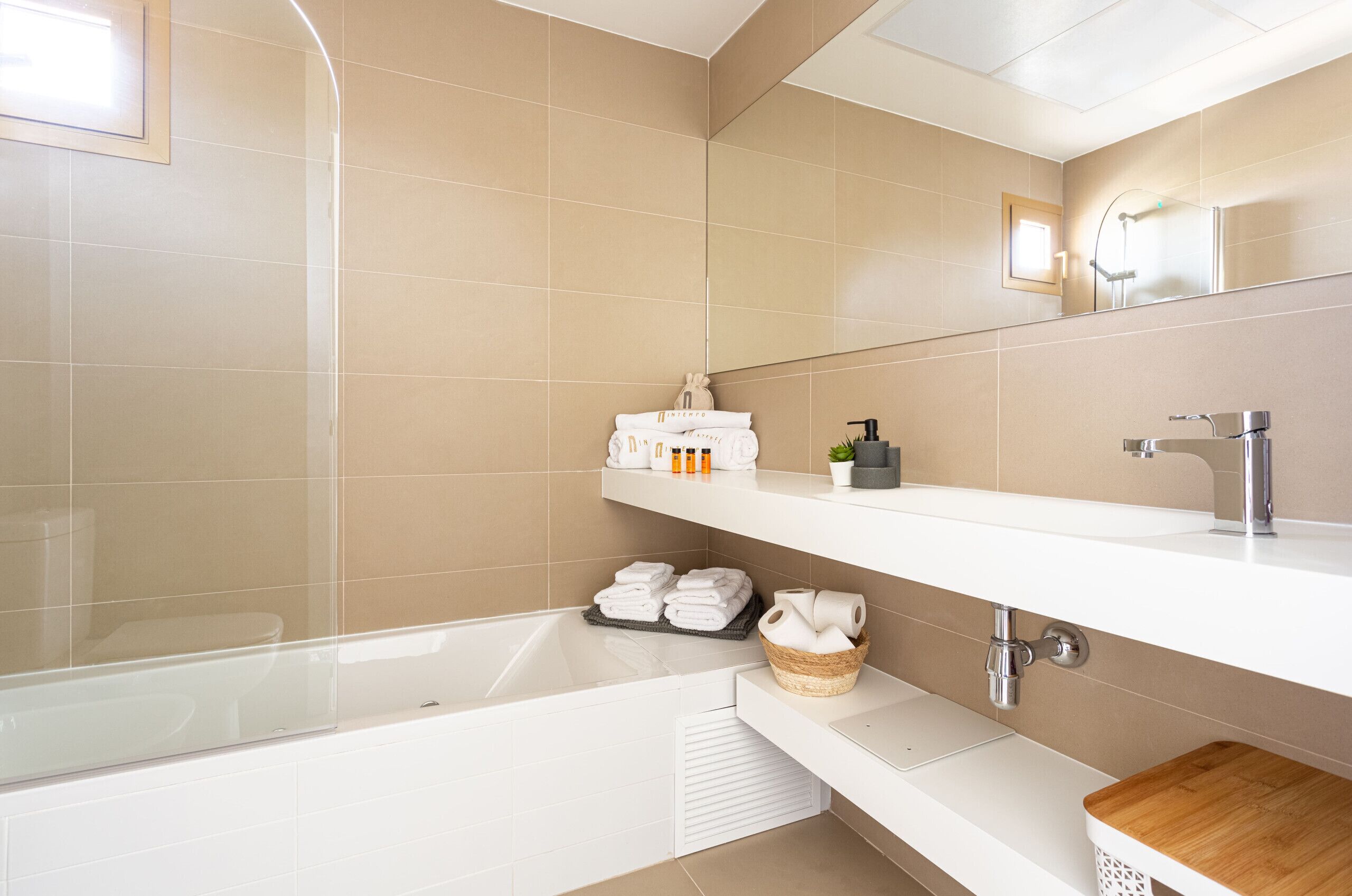 A modern bathroom with a bathtub, a vanity with a mirror, and shelves with toiletries.