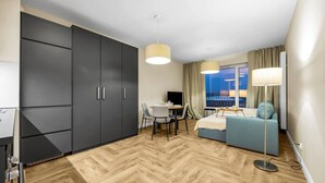 Ein modernes Hotelzimmer mit großem Kleiderschrank, einem Essbereich mit Tisch und Stühlen, einer Couch und einem großen Fenster mit Blick auf die Stadt.