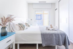 Moderni hotellihuone, jossa on sänky, yöpöytä, lamppu ja ikkunasta avautuva näkymä kaupunkiin.