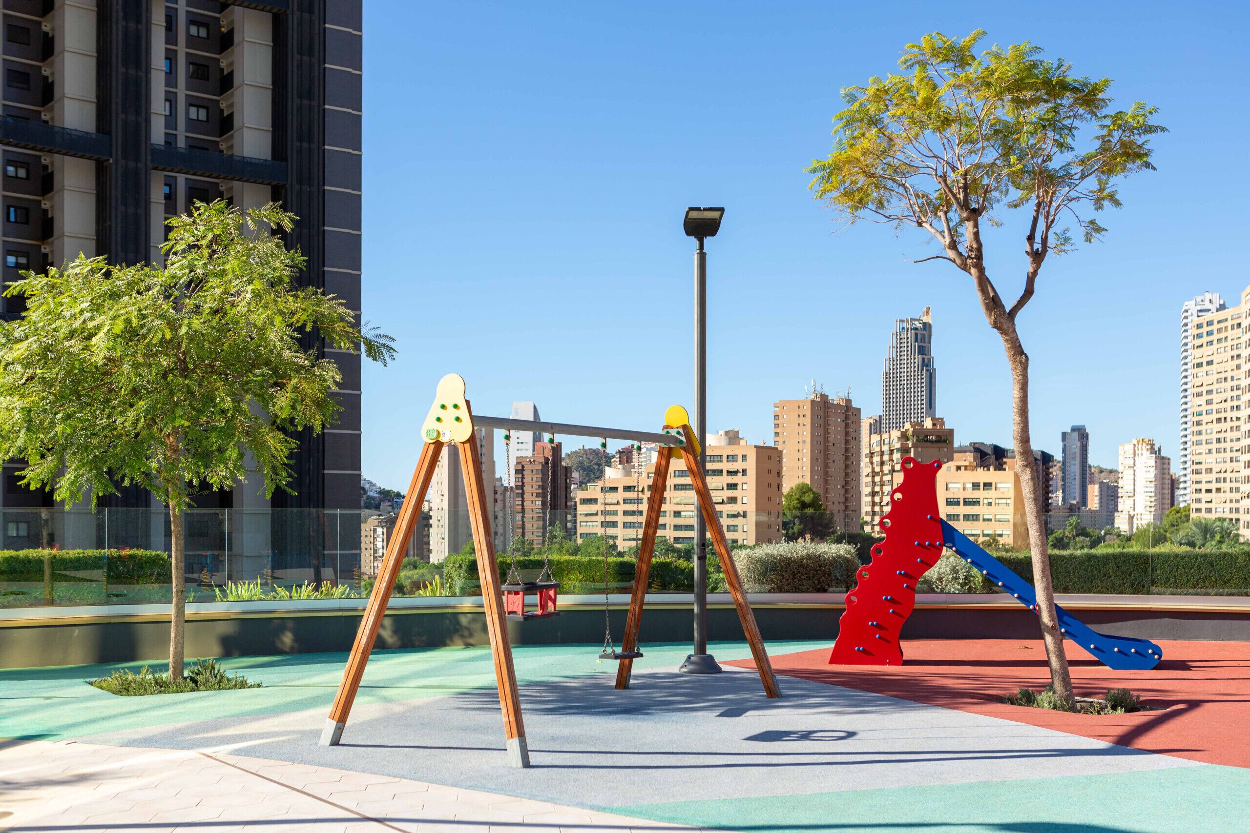 A playground with swings and a slide, surrounded by trees and buildings.