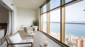 Un balcone con vista sul mare, un'area pranzo con tavolo e sedie e un angolo salotto con divano e pianta.