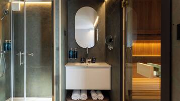 Un baño moderno con cabina de ducha de vidrio, un lavabo blanco con espejo y toallas ordenadas en un estante.