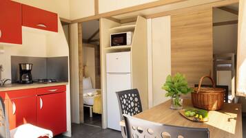 A compact kitchenette with a coffee maker, a microwave, and a refrigerator. There is a dining area with a table, chairs, and a basket with fruits.